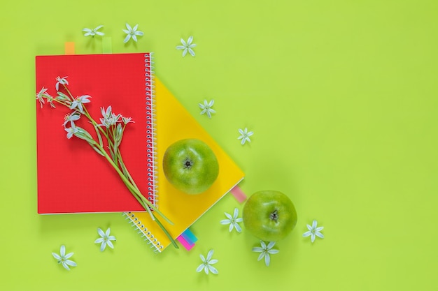 Photo many blossom flower heads ornithogalum and red and yellow notebooks with bouquet green juicy apples on bright green surface