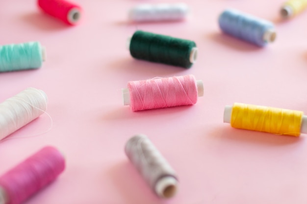 Photo many bobbins of bright sewing thread with a soft pink background