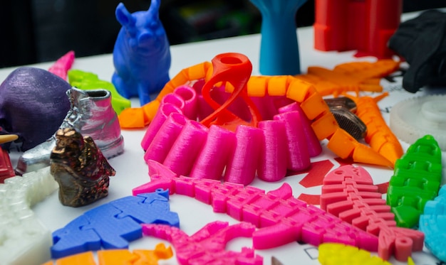 Many bright multi-colored objects printed on 3d printer lie on flat surface close-up. Fused deposition modeling, FDM. Concept modern progressive additive technology for 3d printing.