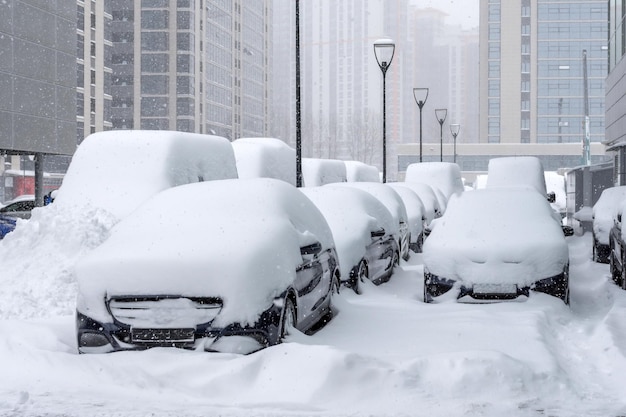 Many cars parked in the business district of the city during a snow storm.