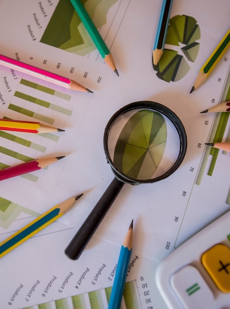 Many charts and graphs with magnifying glass and many pencil. Reflection light and flare. Concept image of data gathering and statistical working.