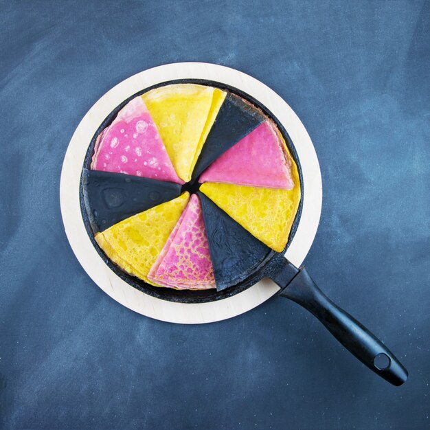 Many colored pancakes on a frying pan.