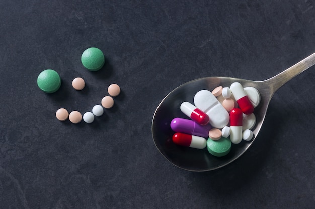 Many colored pills and tabs with spoon on a dark background