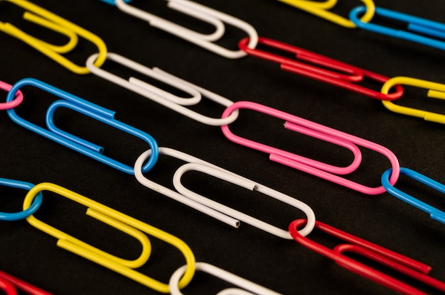 Many colorful paper clips lie on black 