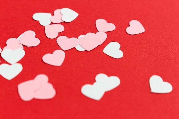 Photo many colorful paper heart shaped confetti on pink or red background.