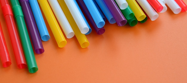 Many colorful straws for drinks lies on a bright orange background surface