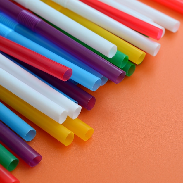 Many colorful straws for drinks lies on a bright orange background surface