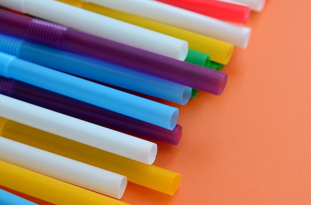 Many colorful straws for drinks lies on a bright orange background surface