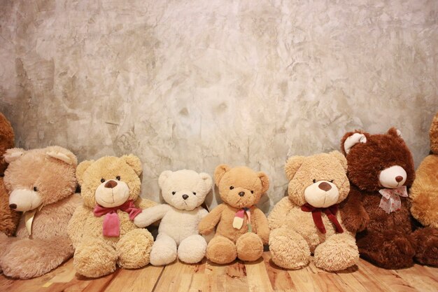 Many cute bear dolls are on the wooden floor with vintage wall.