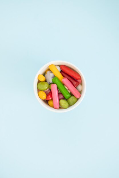 Many different candies sweets in paper cup on blue background