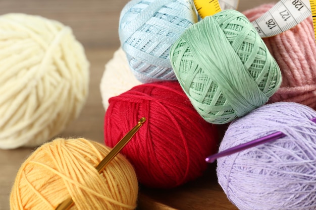 Many different clews of colorful knitting threads measuring tape and crochet hooks on wooden table closeup