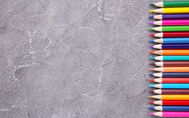 Many different colored pencils on grey concrete background