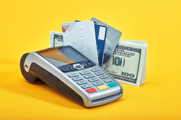 Many different credit cards, dollar bills and payment terminal on yellow background, closeup