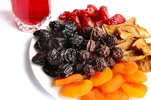 Many different dried fruits (dried apricots, apples, pears, prunes) on a white plate and a glass of compote. Isolated on white background. Multivitamin, antioxidant product.
