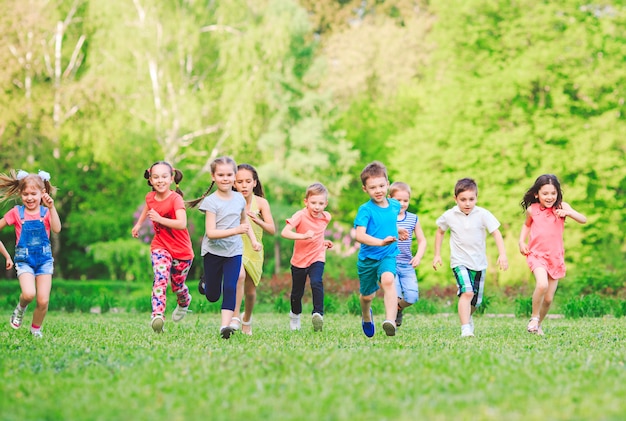 Molti diversi bambini, ragazzi e ragazze che corrono nel parco in giornata di sole estivo in abbigliamento casual