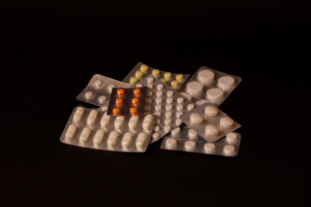 Many different packages of pills, medications, sedatives, antivirals, vitamins on a black background