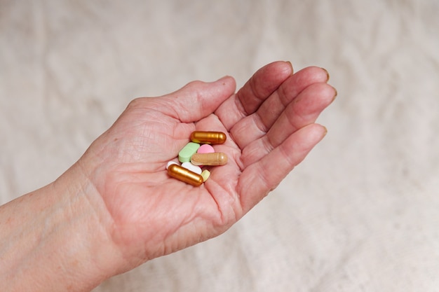 Many different pills in the hand of an elderly person.