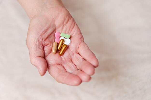 Many different pills in the hand of an elderly person.