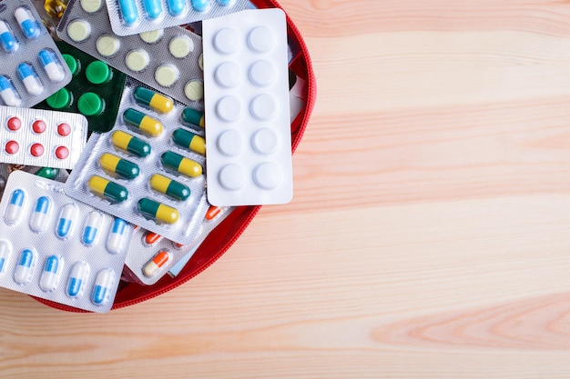 Many different pills in red bag on wooden table with copy space for inscription