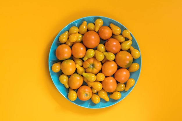 Many different yellow tomatoes on yellow surface Beautiful food art background top view