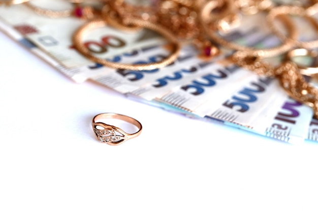 Molti costosi anelli di gioielli d'oro orecchini e collane con una grande quantità di banconote ucraine banco dei pegni o concetto di negozio di gioielli commercio di gioielli