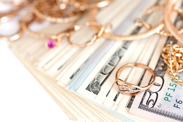 Molti costosi anelli di gioielli d'oro orecchini e collane con una grande quantità di banconote da un dollaro usa su sfondo bianco banco dei pegni o negozio di gioielli