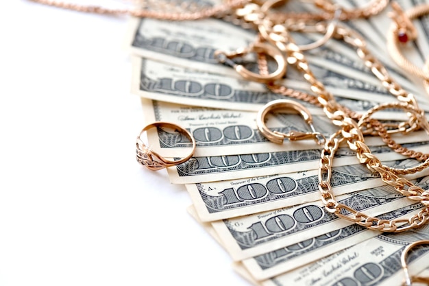 Molti costosi anelli di gioielli d'oro orecchini e collane con una grande quantità di banconote da un dollaro usa su sfondo bianco banco dei pegni o negozio di gioielli