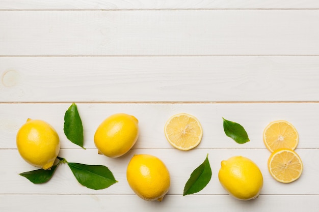 Many fresh ripe lemons with green leaves on colored background top view space for text