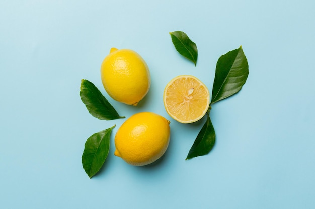 Many fresh ripe lemons with green leaves on colored background top view space for text