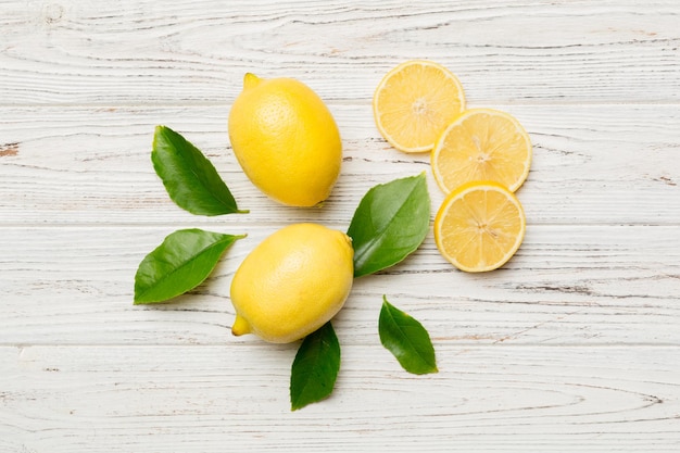 Many fresh ripe lemons with green leaves on colored background top view space for text