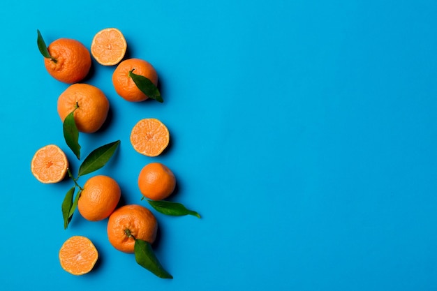 Many fresh ripe mandarin with green leaves on colored background top view space for text