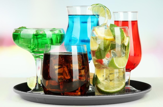 Many glasses of cocktails on tray on table on bright background