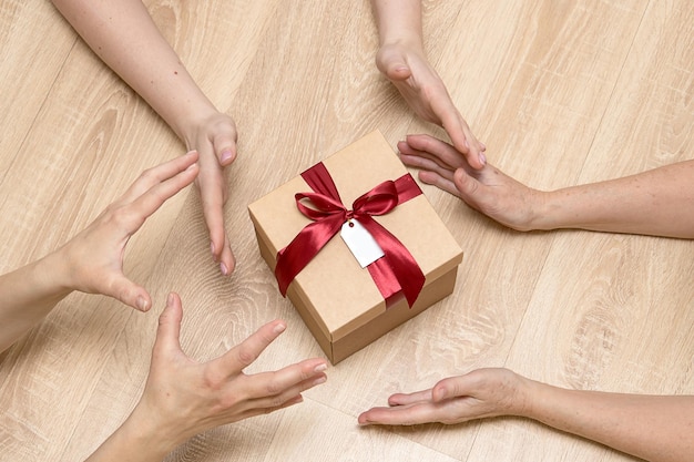 many hands reach for a gift a gift box tied with a bow and an empty tag