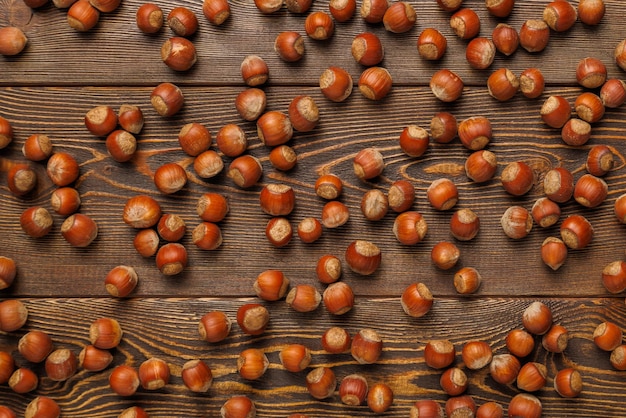 Many hazelnuts with shells evenly spread out on brown wooden surface