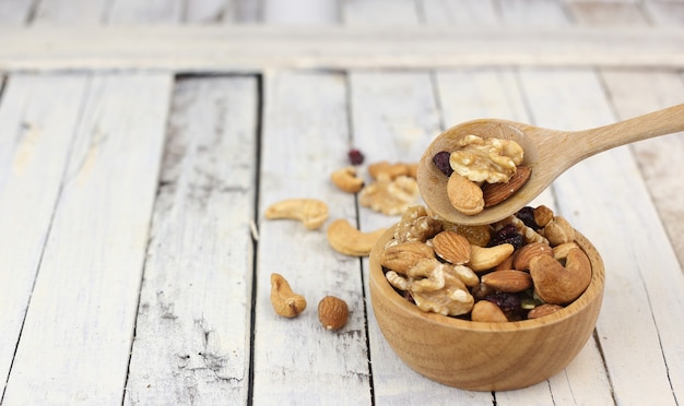 Many healthy nuts on wooden spoon against white wood