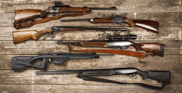 Many hunting rifles on weathered wooden surface