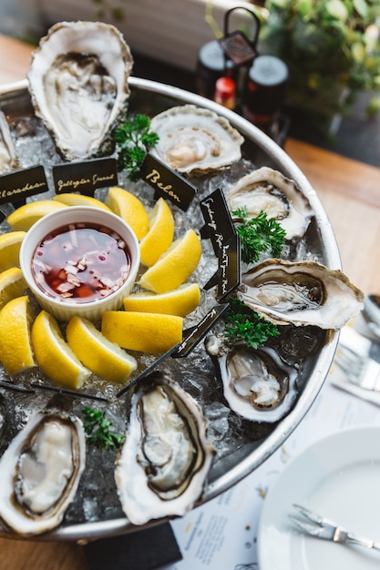 Many kinds of Fresh Oysters served in round tray with slice lemon and spicy sauce.