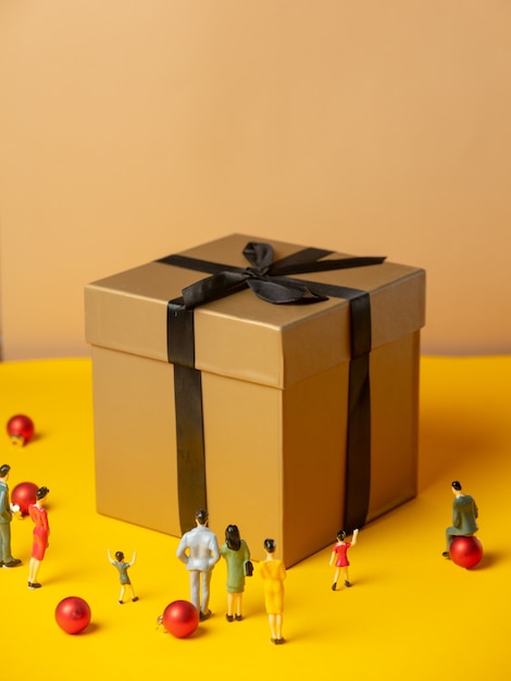 Photo many miniature figures around christmas gift box on yellow surface