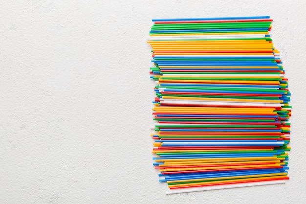 Many multi-colored plastic tubes for cocktail on Colored background, top view.