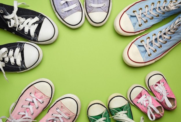 Many multi-colored well-worn textile sneakers of different sizes on a green background, top view, concept, family and team