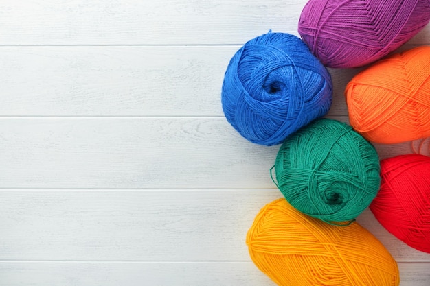 Many multicolored balls of threads on knitted fabric on white wooden backgrounds Yarn of bright colorful flowers knitting and crocheting Needlework or knitting concept