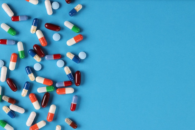 many multicolored medical capsules and pills lying on blue background