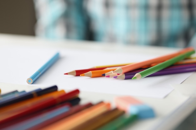 Many multicolored pencils lying on blank sheet of paper closeup