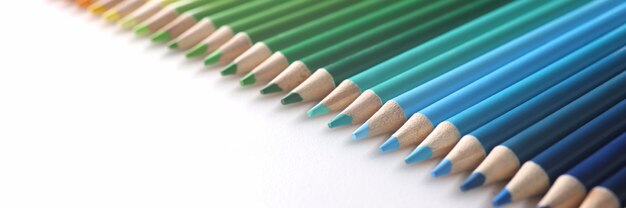 Many multicolored pencils lying in color of rainbow on white background closeup