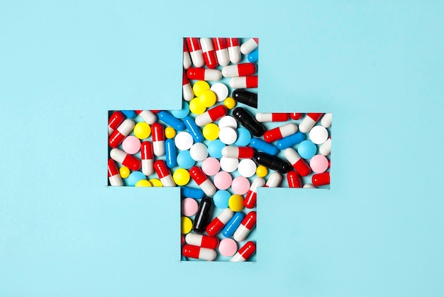 Many multicolored pills on a blue background in the shape of a medical cross