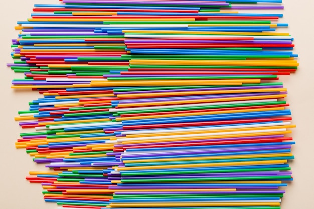 Many multicolored plastic tubes for cocktail on Colored background top view