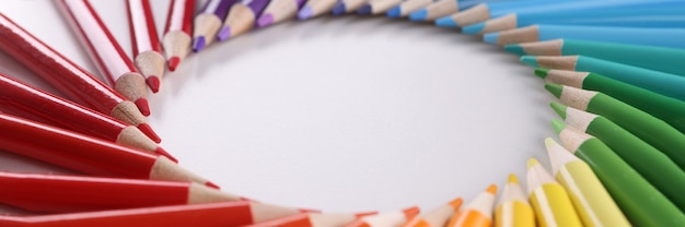 Many multicolored wooden pencils lying in shape of circle over colors of rainbow closeup background