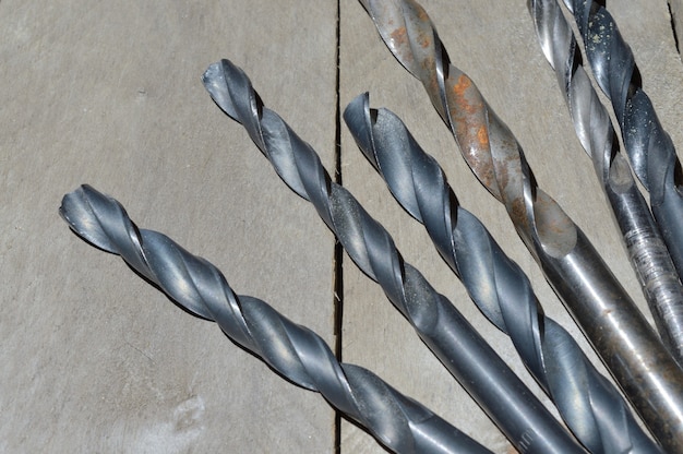 Many old drills lie on a plank wooden background. close-up.