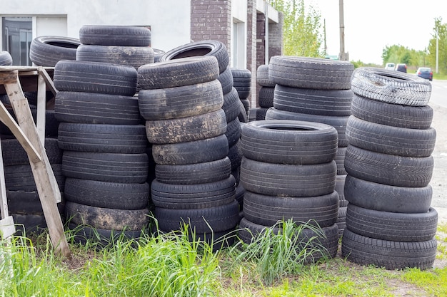 Many old used car tires stacked on top of each other in the grass by the road near the tire shop