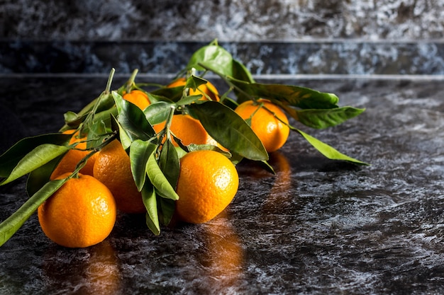 Many orange tangerines with green leaves on dark background. Copy space.